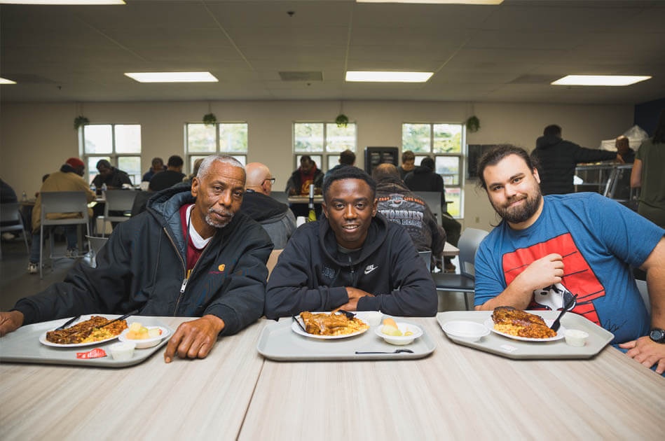 Crossroads men smile and share a meal